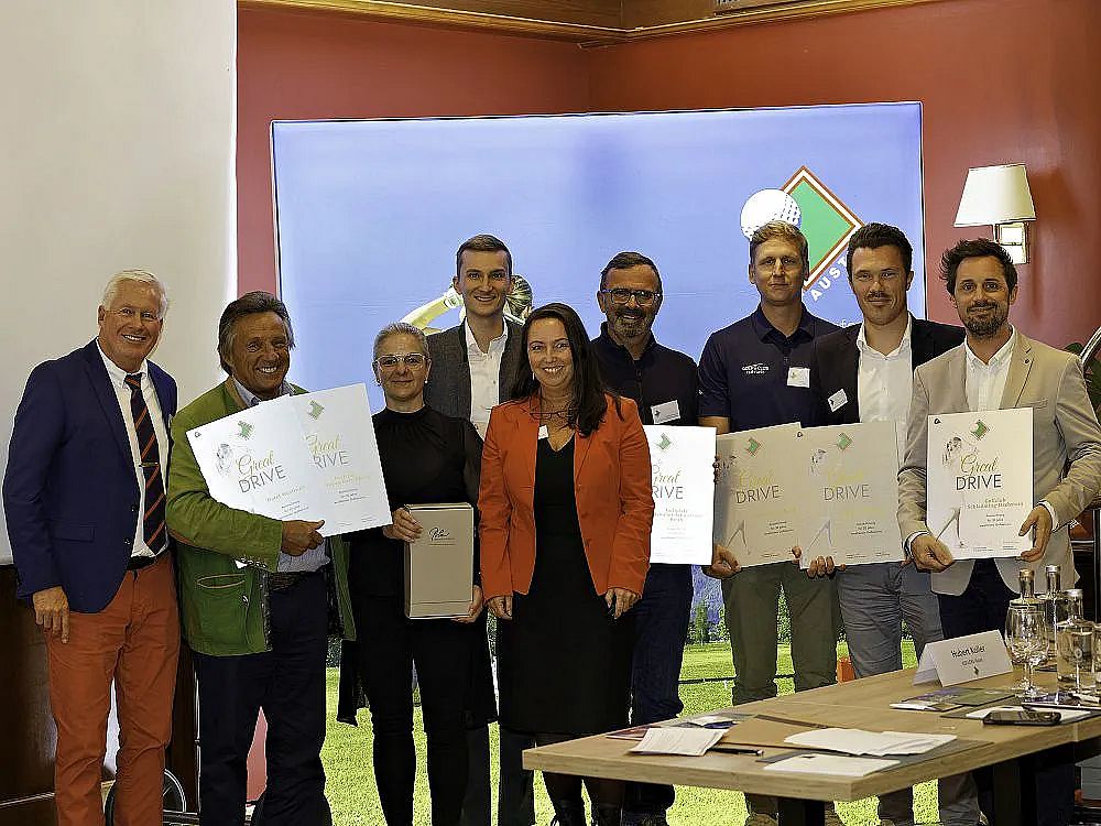 Group of people, including men and women, at an award ceremony. Some hold certificates, all smiling. Indoor setting with a backdrop and a table in view.