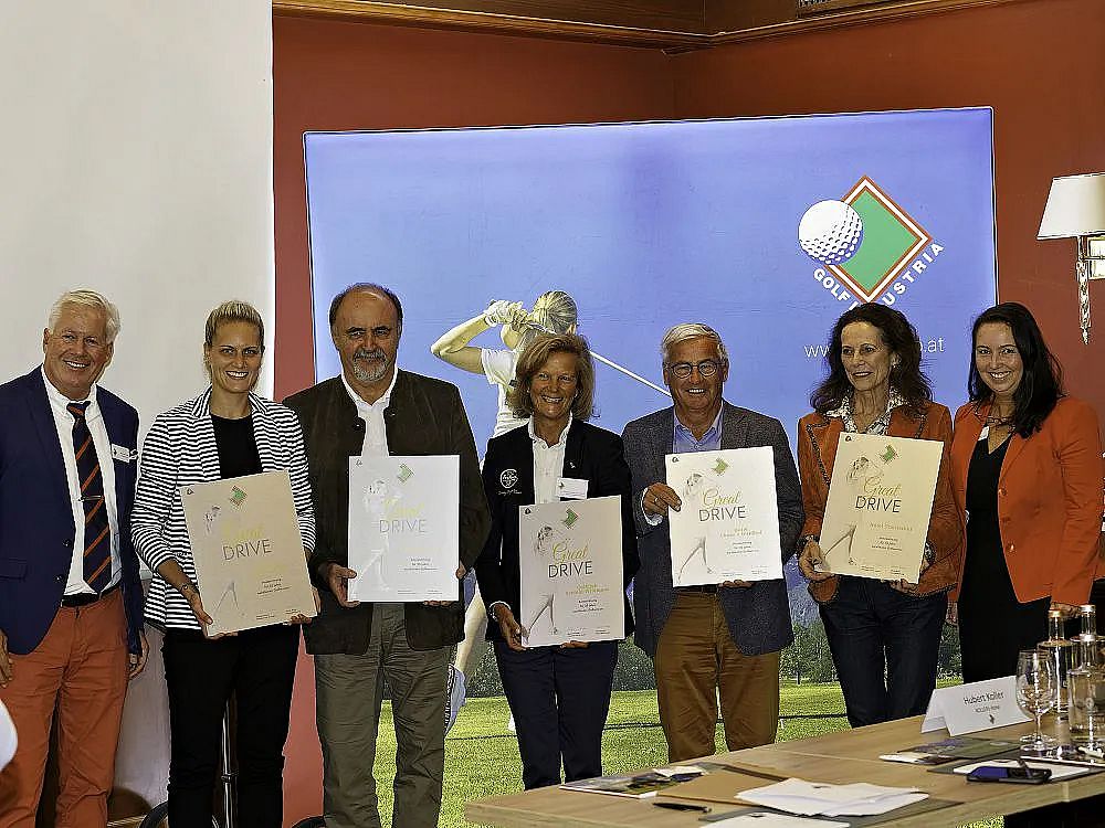 Seven people in formal attire hold certificates, smiling, in front of a background with a golf club logo. They appear to be at an event.