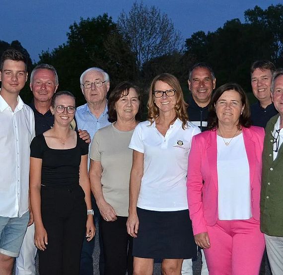 Ten people stand outside, smiling in casual wear. Trees and a dusk sky are visible in the background.