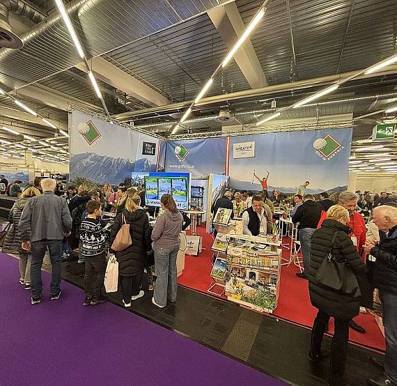 A busy travel expo with people visiting booths showcasing destinations, under bright lights and colorful displays.