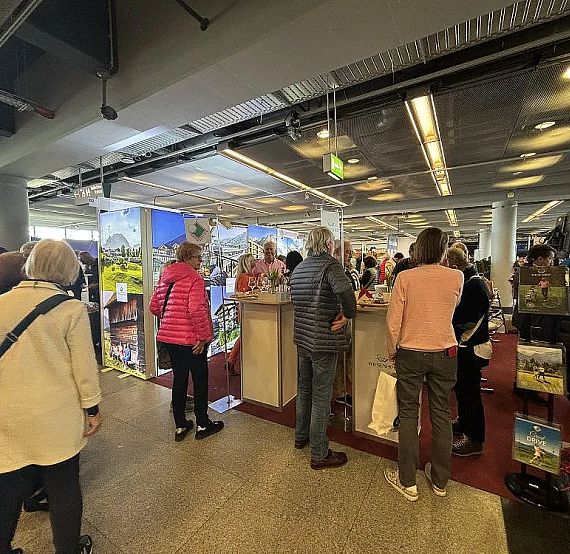Crowd at airport information desk with travelers seeking help, surrounded by signage and travel materials in a busy terminal.