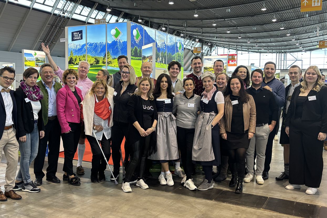 A group of people poses together at an indoor event. They stand smiling in front of a vibrant booth with colorful graphics and signage.