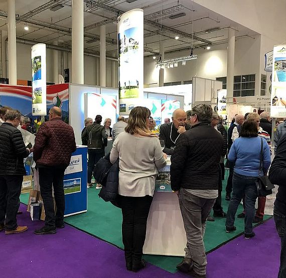 People visiting an indoor trade show with colorful booths and banners, engaging in conversations and examining displays.