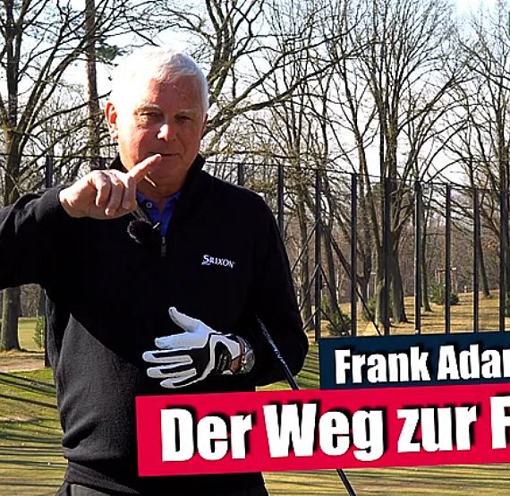 A man in a golf setting gives tips, wearing a black jacket and white glove, pointing forward with bare trees in the background.
