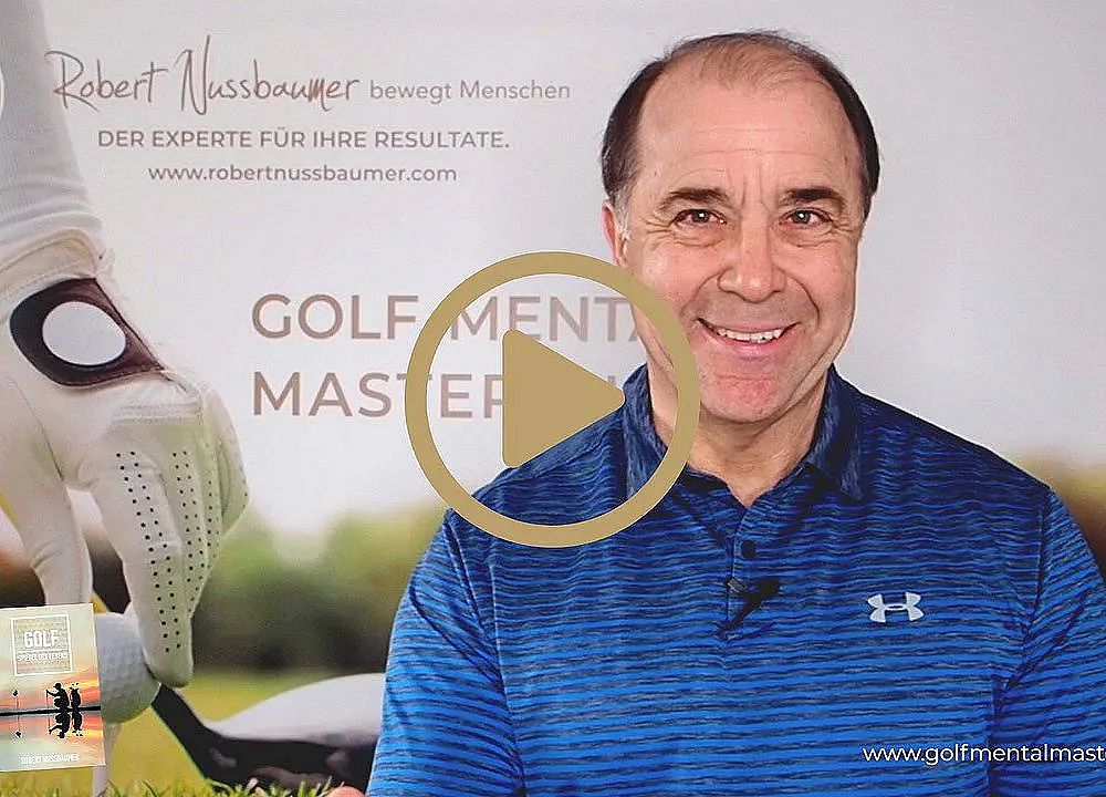 Ein Mann in blauem Hemd lächelt in die Kamera. Im Hintergrund ist ein Plakat mit Text über Golfmentoring zu sehen. Es wirkt wie ein Videovorschaubild.