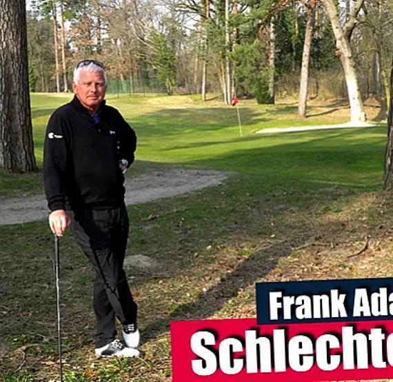 A golfer stands on a grass course with trees, holding a club, facing the camera, on a sunny day.