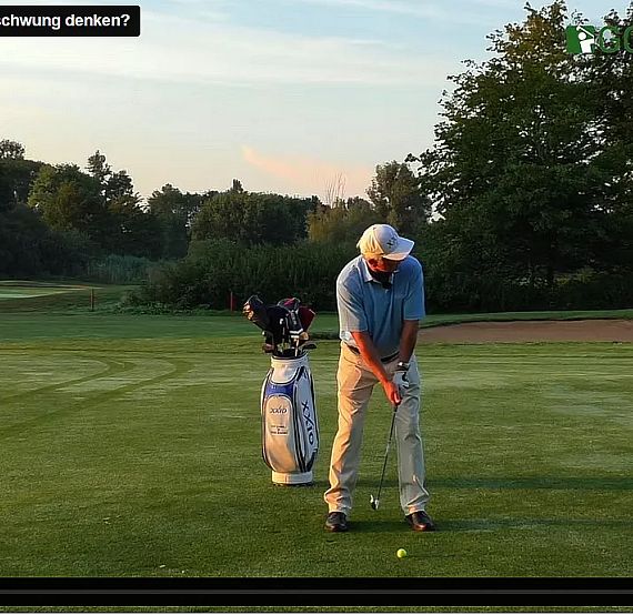 Golfer on a green course lining up for a shot, sunset in the background, wearing casual golf attire and a cap.