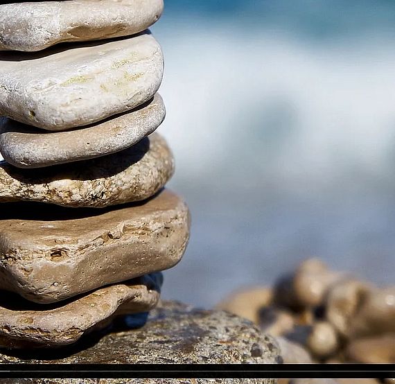 A stack of smooth, flat stones is balanced on a rocky beach, with a blurry ocean in the background, creating a peaceful and serene atmosphere.