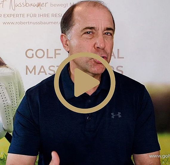 A man in a blue polo shirt gestures while speaking, with a golf-themed background featuring a glove and a golf ball on grass.