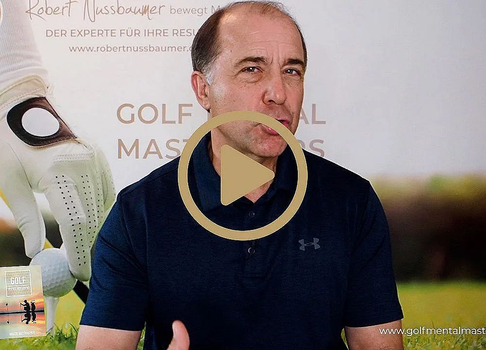 A man in a blue polo shirt gestures while speaking, with a golf-themed background featuring a glove and a golf ball on grass.