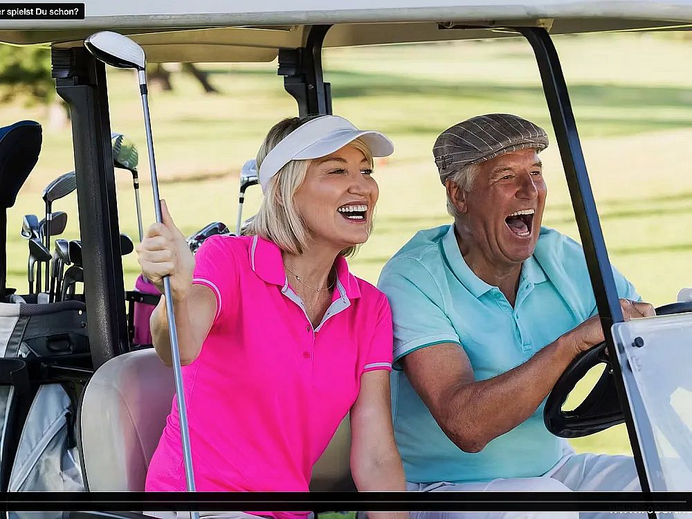 Elderly couple in a golf cart, woman holding a club, both laughing in sporty attire. Sunny golf course background.