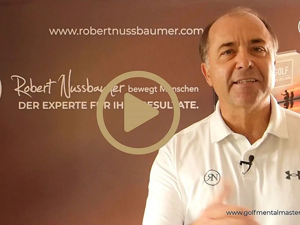 Älterer Mann mit weißem Polohemd steht vor einer Präsentationswand, lächelt und gestikuliert. Sein Name ist auf der Wand hinter ihm sichtbar. Webadresse unten.