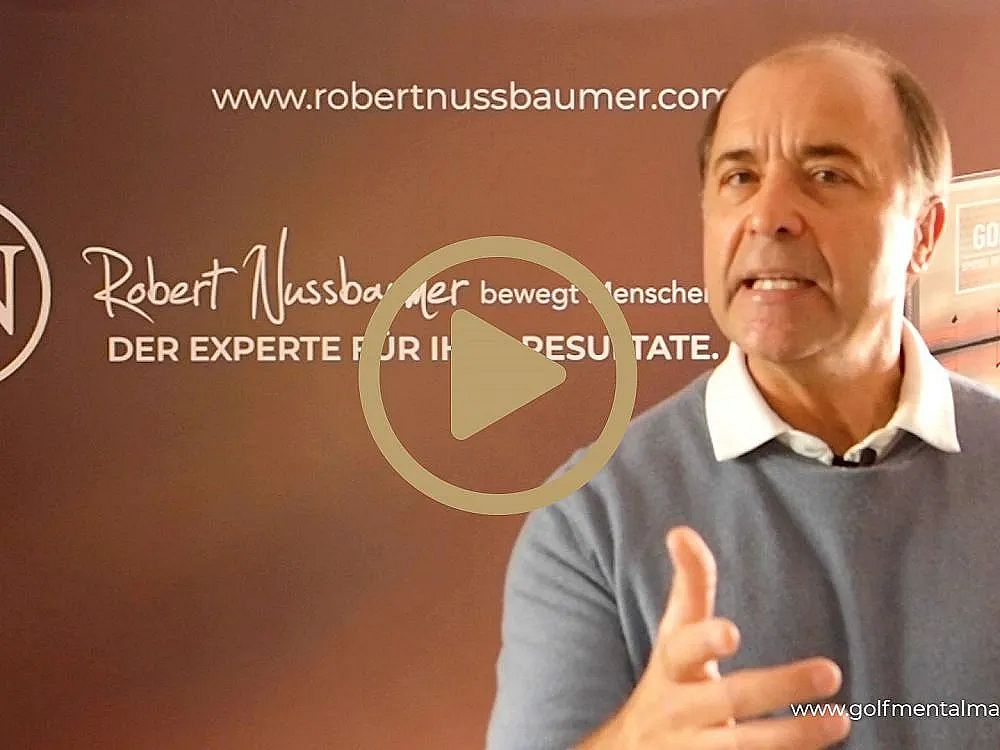A man makes a motivational speech in front of a branded backdrop. He is gesturing with one hand, engaged in delivering his message passionately.
