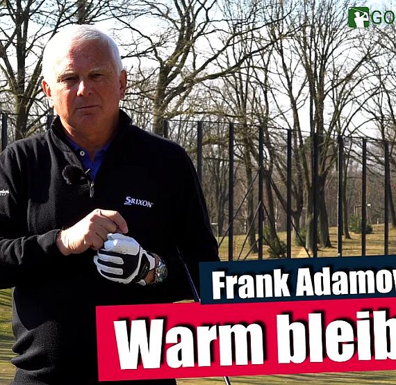 A man in a golf course setting wearing a black jacket with trees in the background, holding a glove. Text overlay says 'Warm bleiben'."