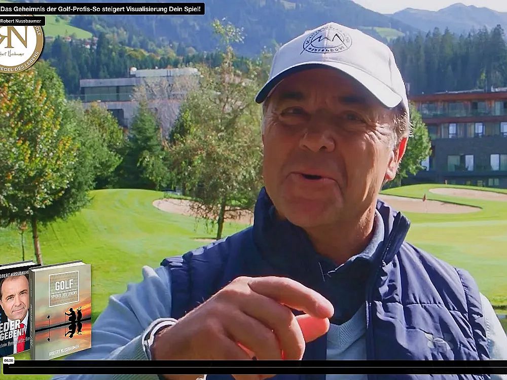 Person in a cap on a sunny golf course speaking to the camera, surrounded by greenery and buildings in the background.