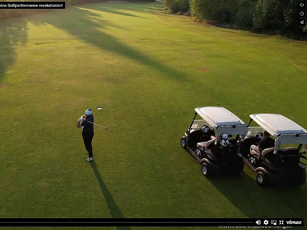 A golfer stands on a green field ready to swing, two golf carts nearby under a clear sky, infused with warm morning light.