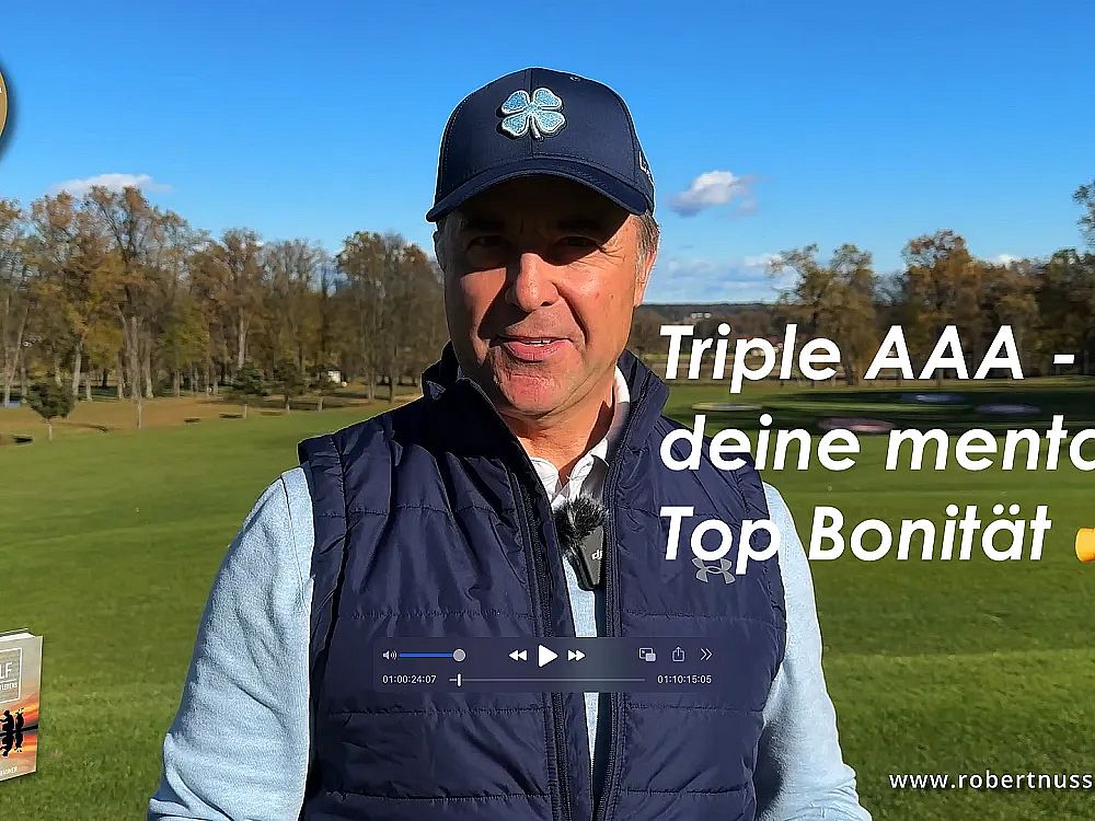 Ein Mann steht auf einem Golfplatz. Er trägt eine blaue Mütze und eine Weste. Im Hintergrund sind Bäume und ein klarer Himmel zu sehen.