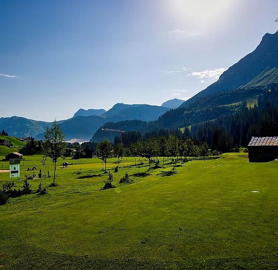 A picturesque mountain landscape with green fields, small trees, and distant hills under a clear sky, creating a peaceful and serene atmosphere.