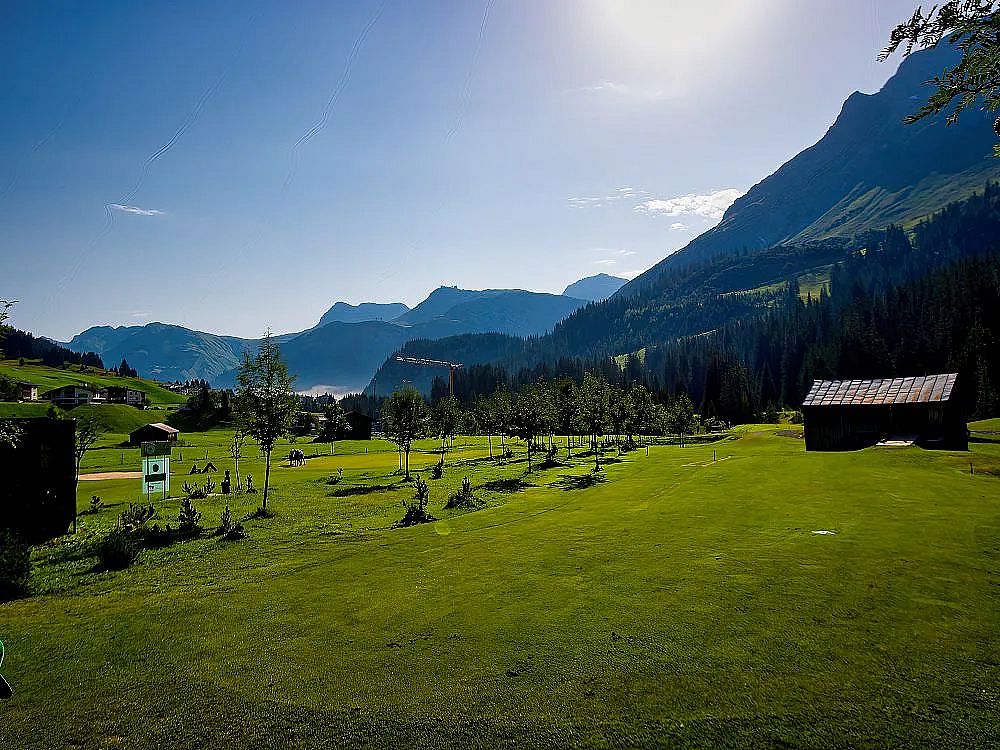 A picturesque mountain landscape with green fields, small trees, and distant hills under a clear sky, creating a peaceful and serene atmosphere.