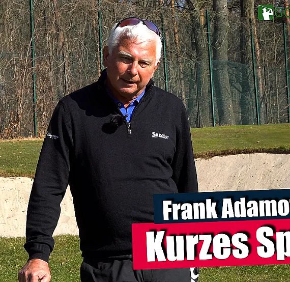 An older man stands on a golf course near a sand trap, discussing short game strategies. He looks engaged, offering insights to improve golfing skills.