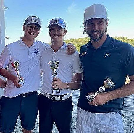 Three men in golf attire holding trophies, smiling on a sunny day on a wooden deck, indicating a successful event or competition.